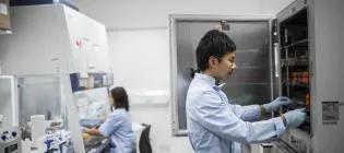 Scientist in a lab coat retrieving something from an incubator