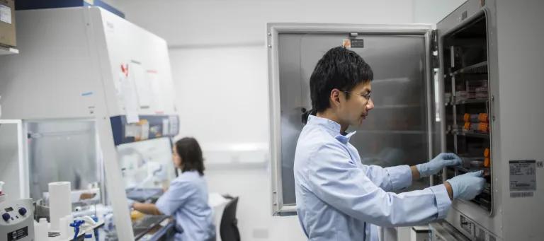 Scientist in a lab coat retrieving something from an incubator