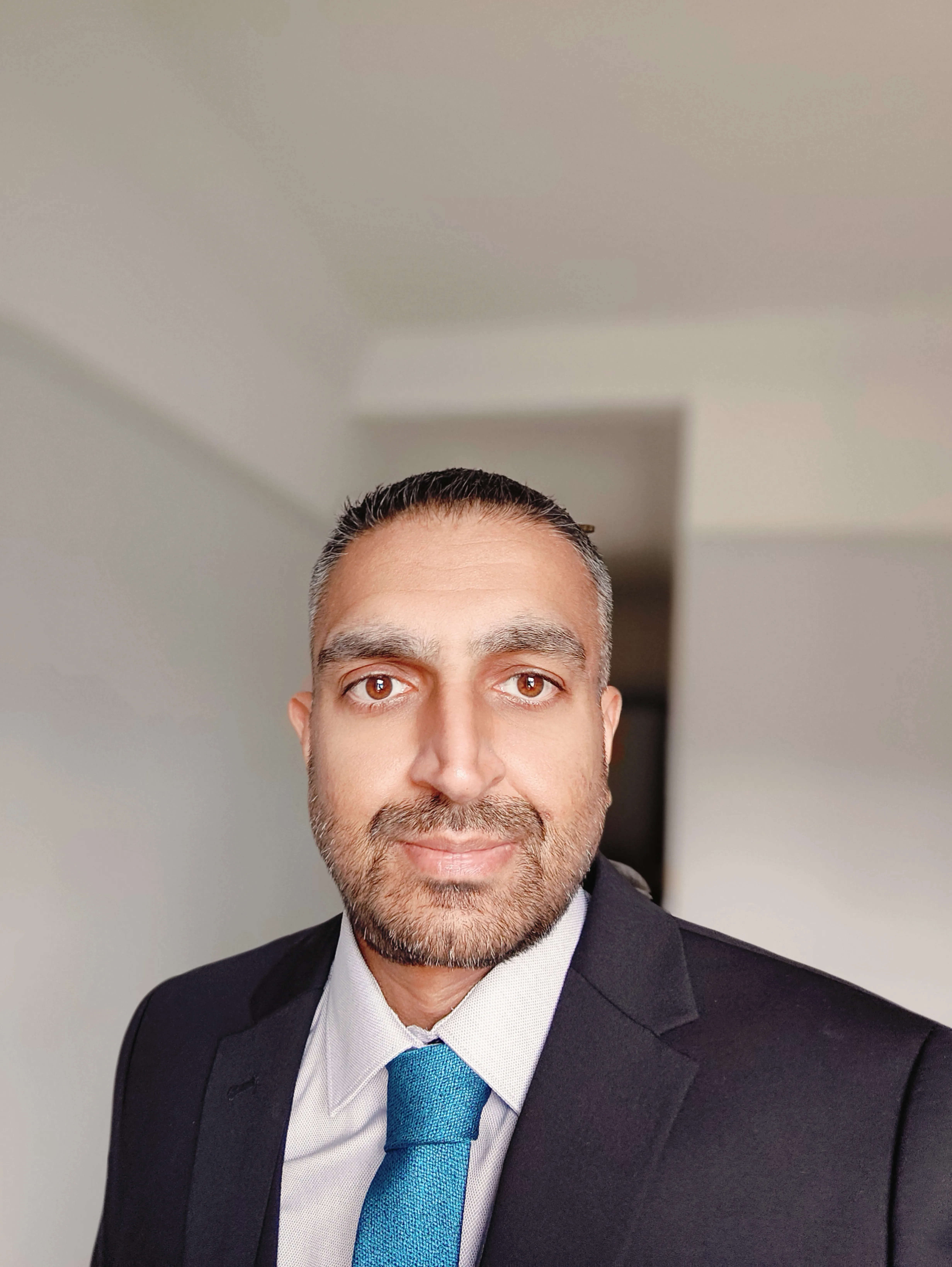 Dr Ahsan Akram wears a dark suit and light blue tie, smiling at the camera
