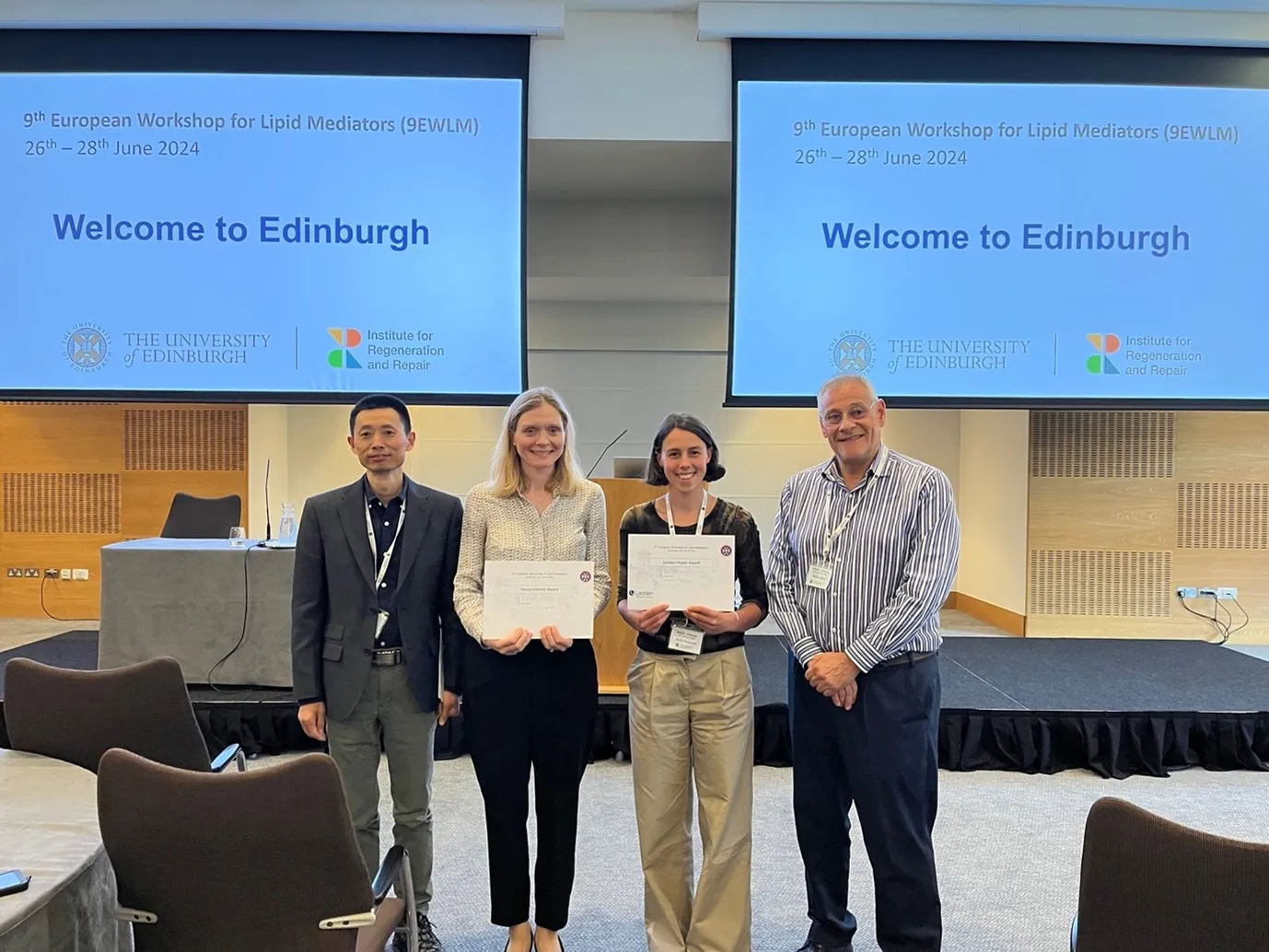 Four people, the middle two holding certificates, stand in front of projector screens showing the cover slide for the workshop