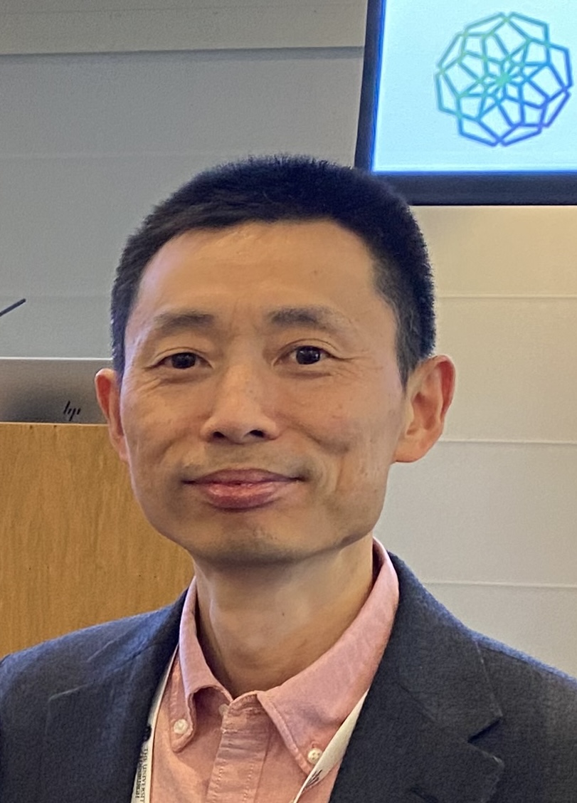 A portrait photo of man with short hair, wearing a pink shirt and blue blazer.